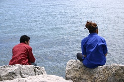 two people sitting on rocks looking out over the water
