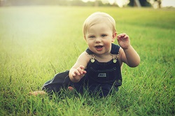 Happy toddler in coveralls sitting in the grass